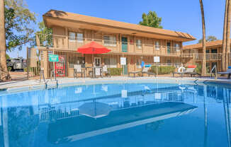 A swimming pool in front of a building with a red umbrella.