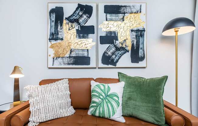 A brown couch with two green and one white pillow with a painting in the background.