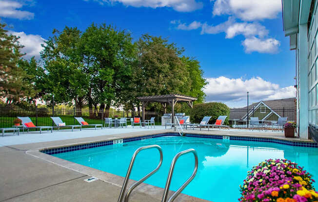 A pool with a diving board and chairs around it.
