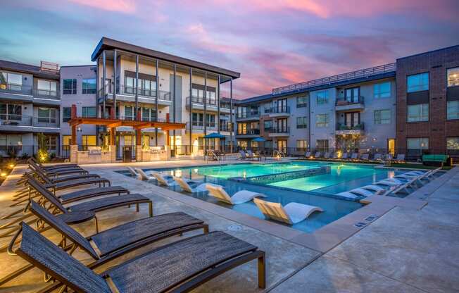 an apartment pool with lounge chairs at dusk