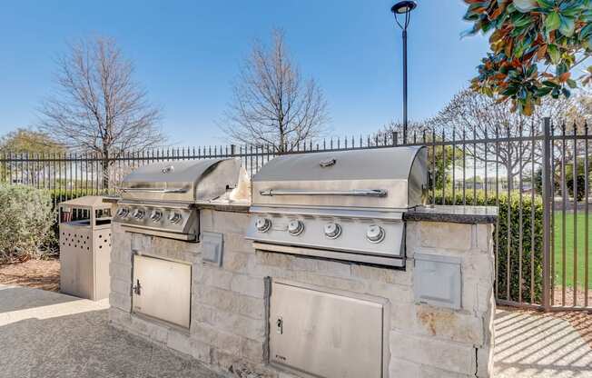 an outdoor kitchen with two gas grills and two trash cans