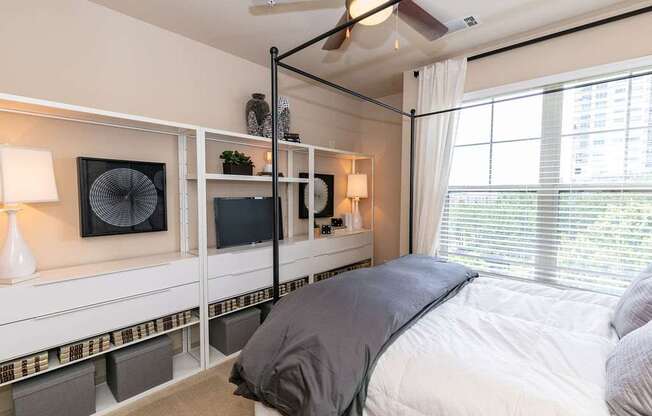 A bedroom with a bed, a fan, and a window with blinds.