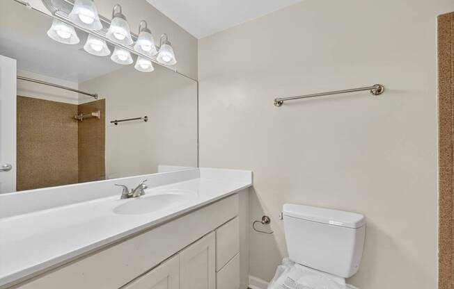 A white toilet sits in a bathroom with a white sink and mirror.