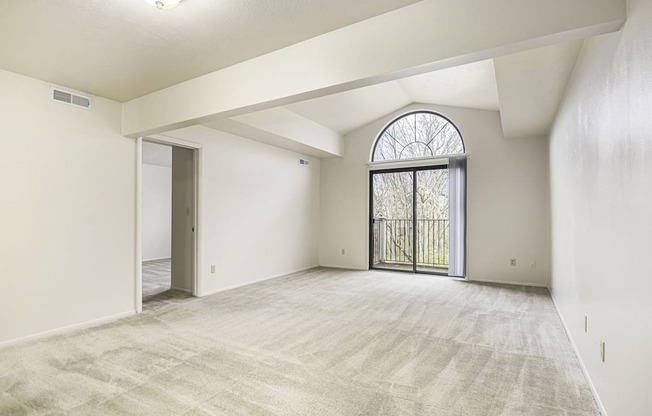 an empty living room with a large window and a door to a balcony