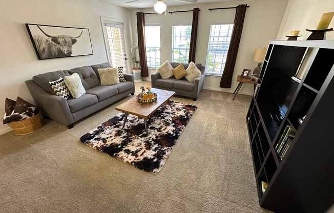 A living room with a grey couch, a black and white cow print rug, and a black entertainment center.