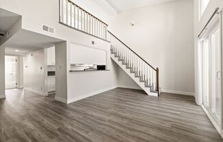 an empty living room with a staircase and a kitchen in the background