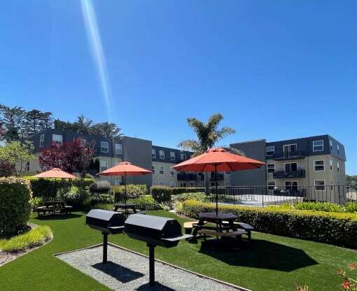 a park with picnic tables and umbrellas in front of an apartment building