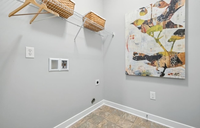 A room with a large painting on the wall and a wooden hanger with a basket on top of a clothes rack.