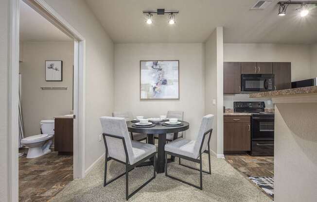 A dining room with a table set for two and a kitchen area in the background.