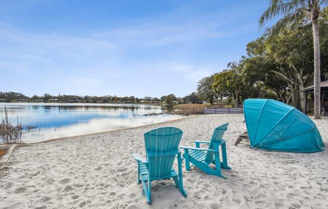 a couple of blue adirondack chairs sitting on top of a sandy beach