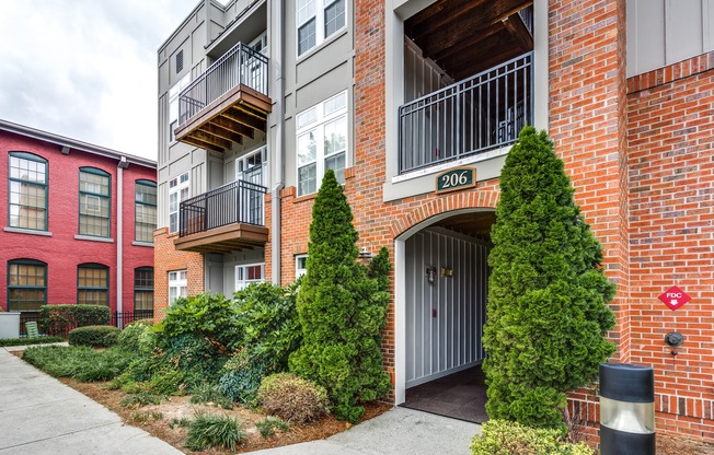 View of Building Exterior, Showing Landscaping, Patios, Balconies, and Entrance at Alpha Mill Apartments