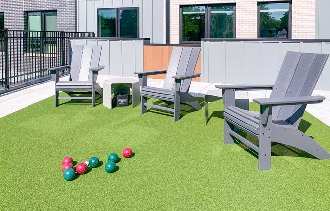 a set of bocce balls in front of Adirondack chairs on a green turf