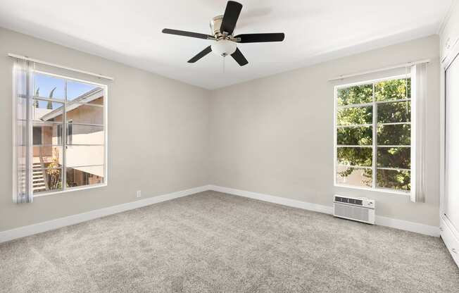 an empty living room with a ceiling fan and two windows