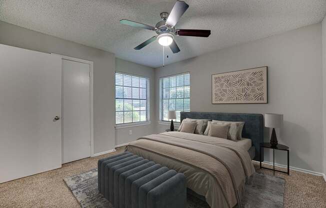 A bedroom with a bed, pillows, a ceiling fan, and a window with blinds.