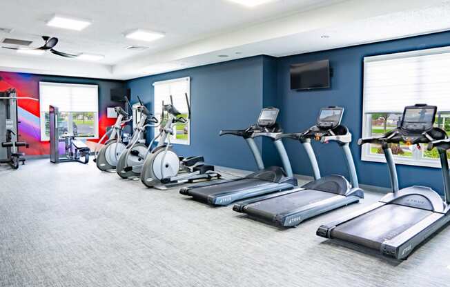 a gym with cardio machines and a television