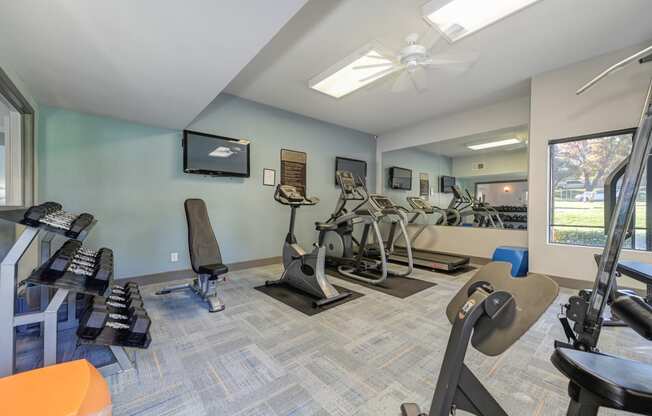 Community Fitness Center.  The Room has a light blue accent wall and contains a weight system, elliptical machines, treadmill, bench and free weights.
