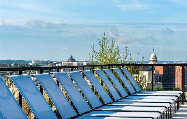 a row of blue lawn chairs are lined up on a balcony with a view of the city