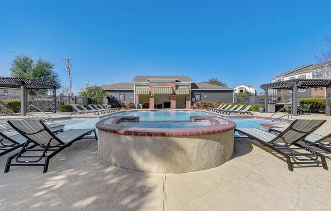 a pool with chairs and a hot tub with a building in the background