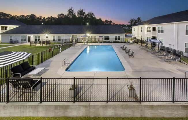 a swimming pool with chairs and tables around it at night