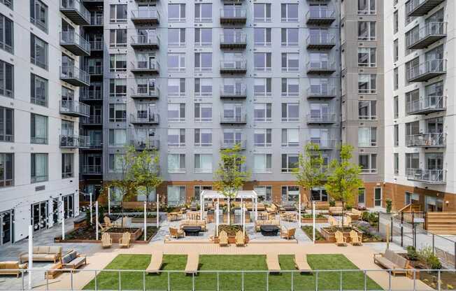 A large grassy area with benches and a pavilion is surrounded by apartment buildings.