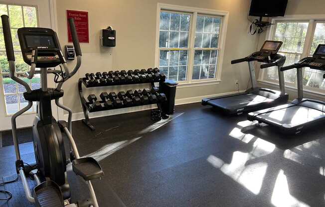 A gym with treadmills, elliptical machines, and dumbbells.