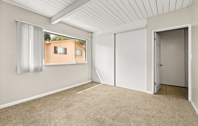 A room with a carpeted floor and a window showing a building outside.
