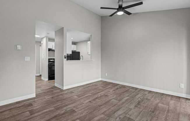 an empty living room with a ceiling fan and a kitchen