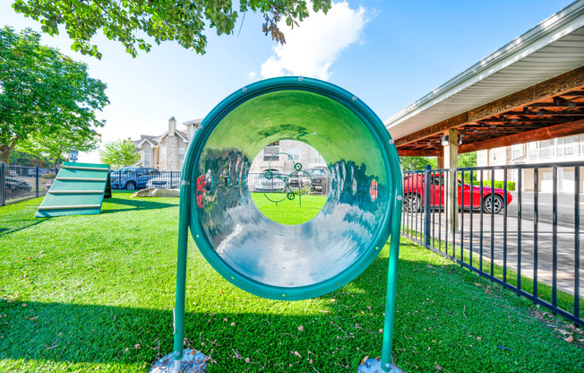 a large metal mirror in a grassy area with a playground in the background
