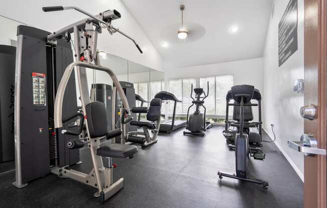 a gym with weights and cardio equipment on the floor and a window