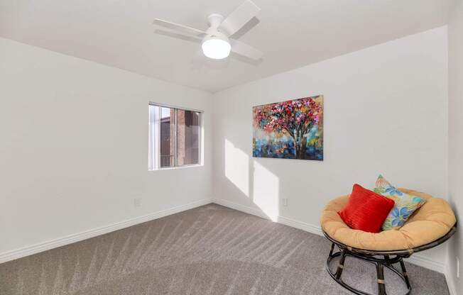 A room with a ceiling fan, a window, a carpeted floor, a chair with a cushion and a painting on the wall at Urban WalkApartments on 6th Avenue, Phoenix, Arizona