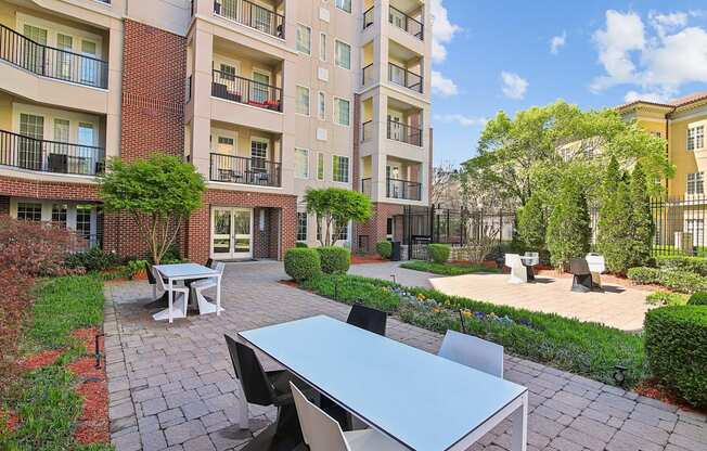 A patio with a table and chairs is surrounded by a brick building and greenery.