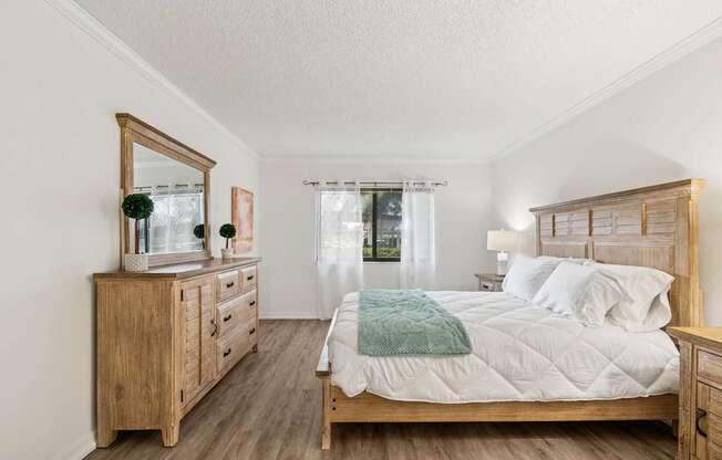 A bedroom with a large bed, a dresser, and a mirror at Hampton Apartments, Clearwater, FL, 33759