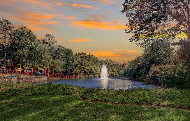 a fountain in the middle of a pond at sunset
