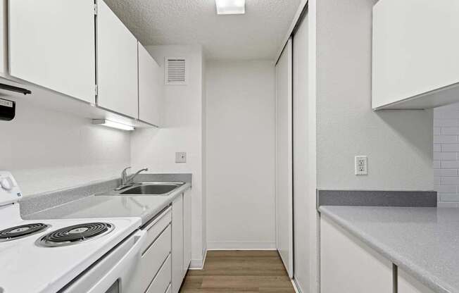 A white kitchen with a stove, sink, and cabinets.
