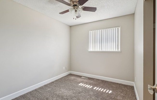 A room with a ceiling fan and a window with blinds.