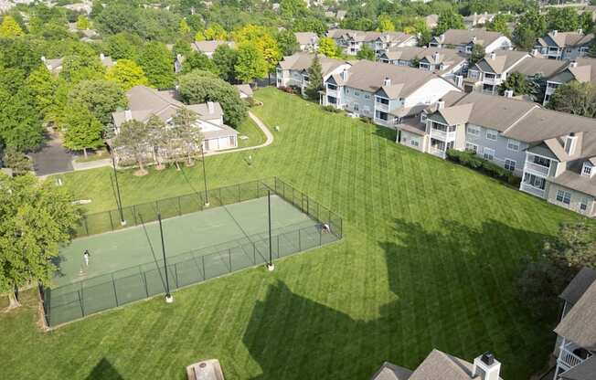 A tennis court is surrounded by houses and trees.