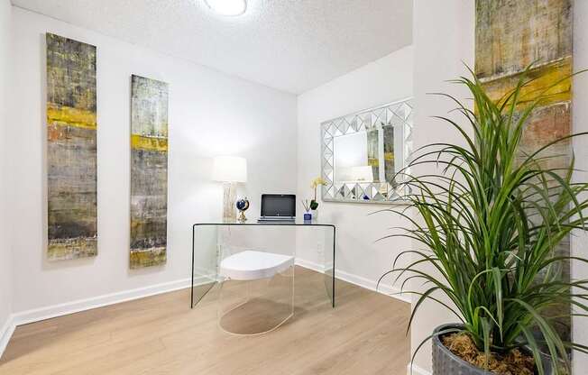 A room with a glass table, a mirror, and a potted plant.