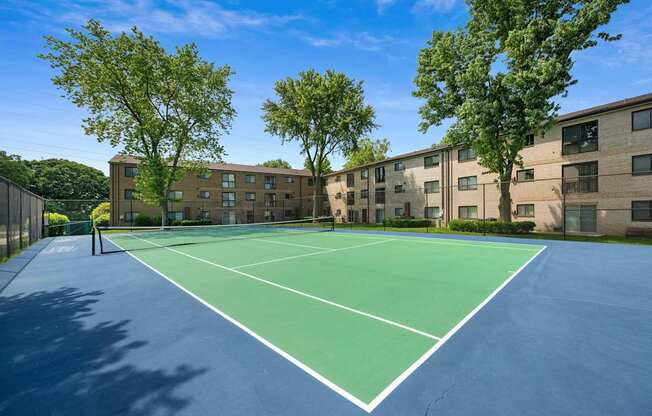 A tennis court is surrounded by apartment buildings.