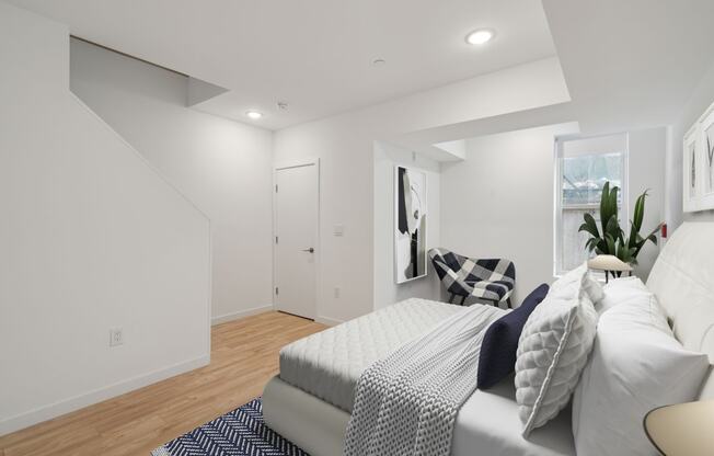 Compact bedroom with a comfortable bed with navy and white bedding, plush pillows, a white fluffy rug, and a plant by the window, creating a serene and inviting atmosphere.