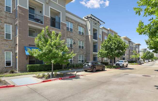 A street view of GreenVue Apartments with lush trees and street parking in Richardson, TX