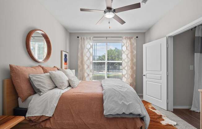 A bedroom with a bed, a ceiling fan, and a window with curtains.
