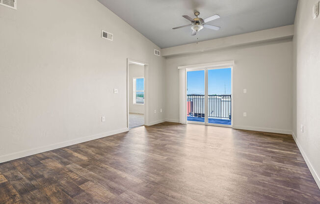 an empty living room with a ceiling fan and a balcony