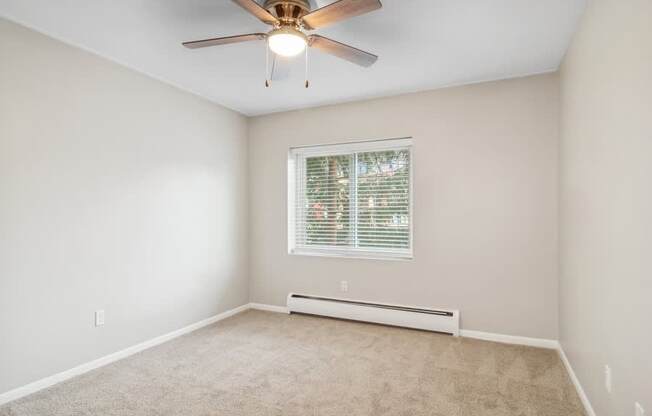 A room with a ceiling fan and a window with blinds.