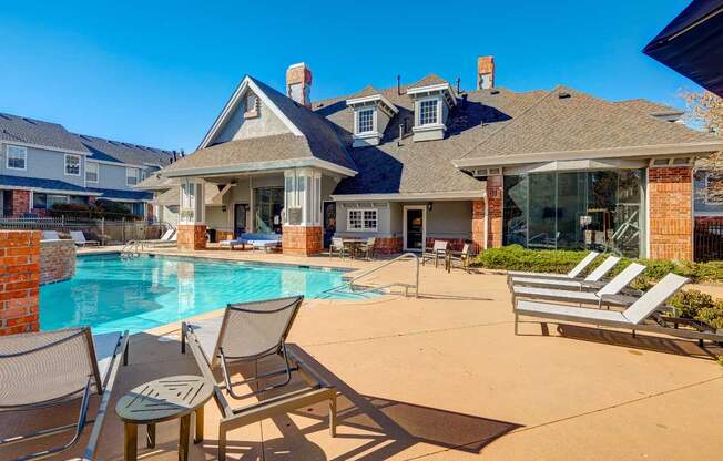 a swimming pool with chairs and a house in the background