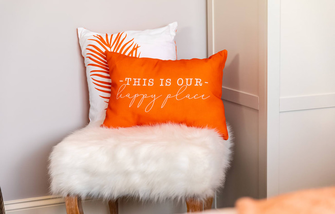 a orange and white pillow sitting on a chair with a white furry seat