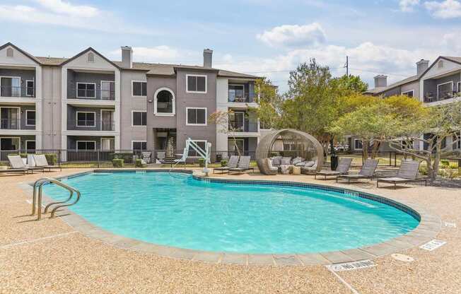 A large swimming pool is surrounded by a concrete patio and chairs.