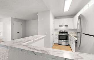 A modern kitchen with a marble countertop and stainless steel appliances.