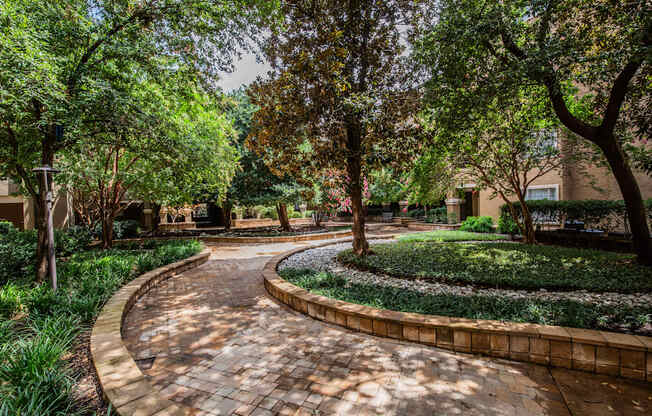 A curved brick pathway leads through a landscaped area with trees and shrubs.