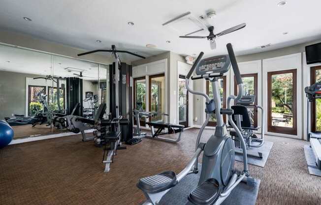 Spacious gym featuring mirrored wall, cable station, and cardio equipment by windows.