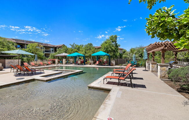 a swimming pool with chairs and umbrellas in front of a house at Lakeline East Apartments, Cedar Park, TX
